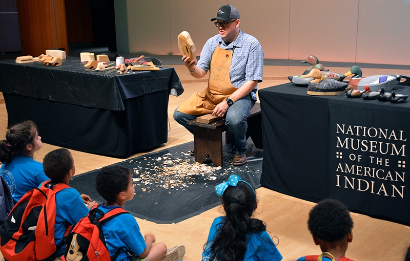 Young visitors from a New York City area summer camp watch as Joshua Hinson creates a duck decoy during a live exhibition at the National Museum of the American Indian.
