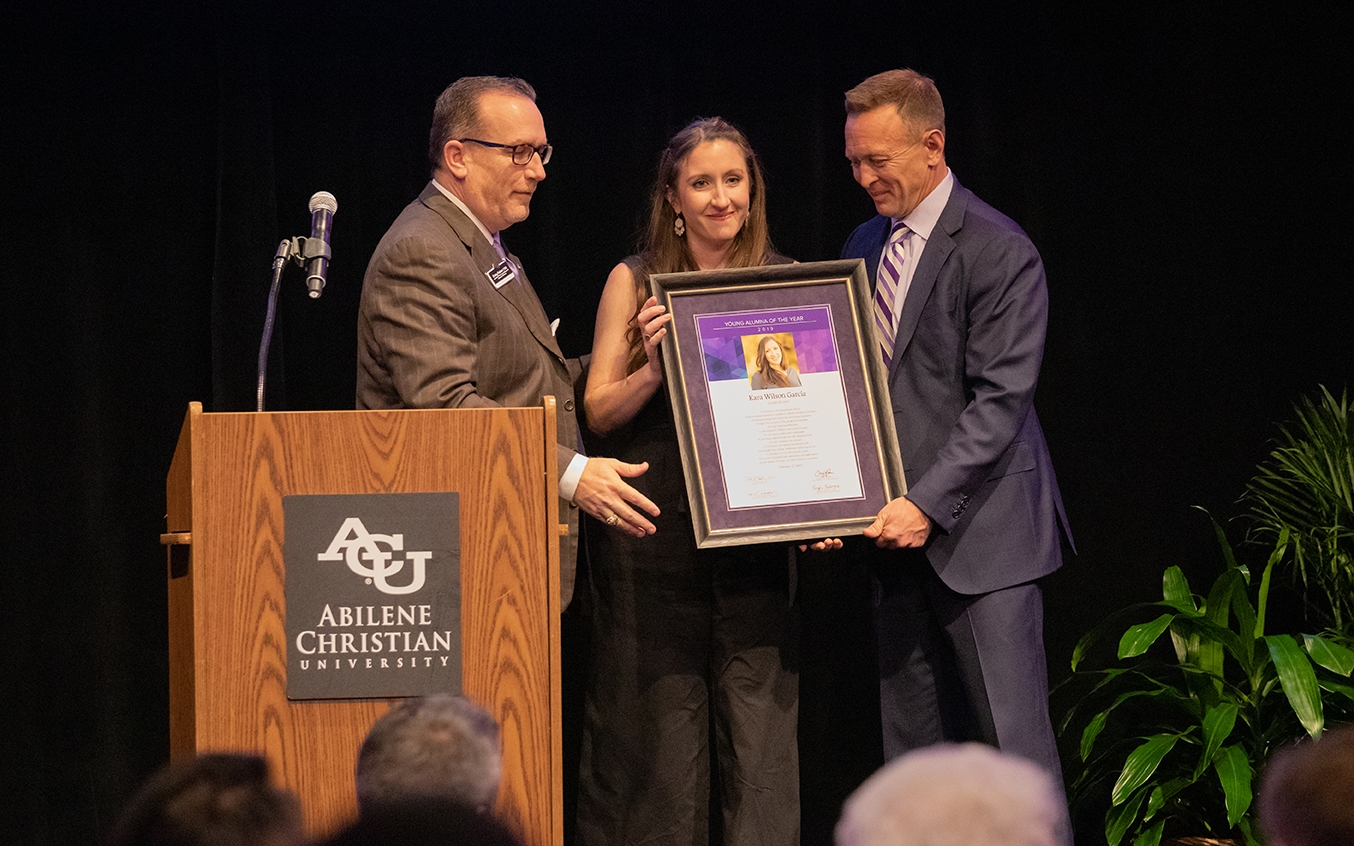 Wilson García receives her Young Alumna of the Year certificate at the Alumni Day luncheon Feb. 17, 2019, from Craig Fisher ('92) (left), assistant vice president of alumni and university relations, and Dr. Phil Schubert ('91), president.